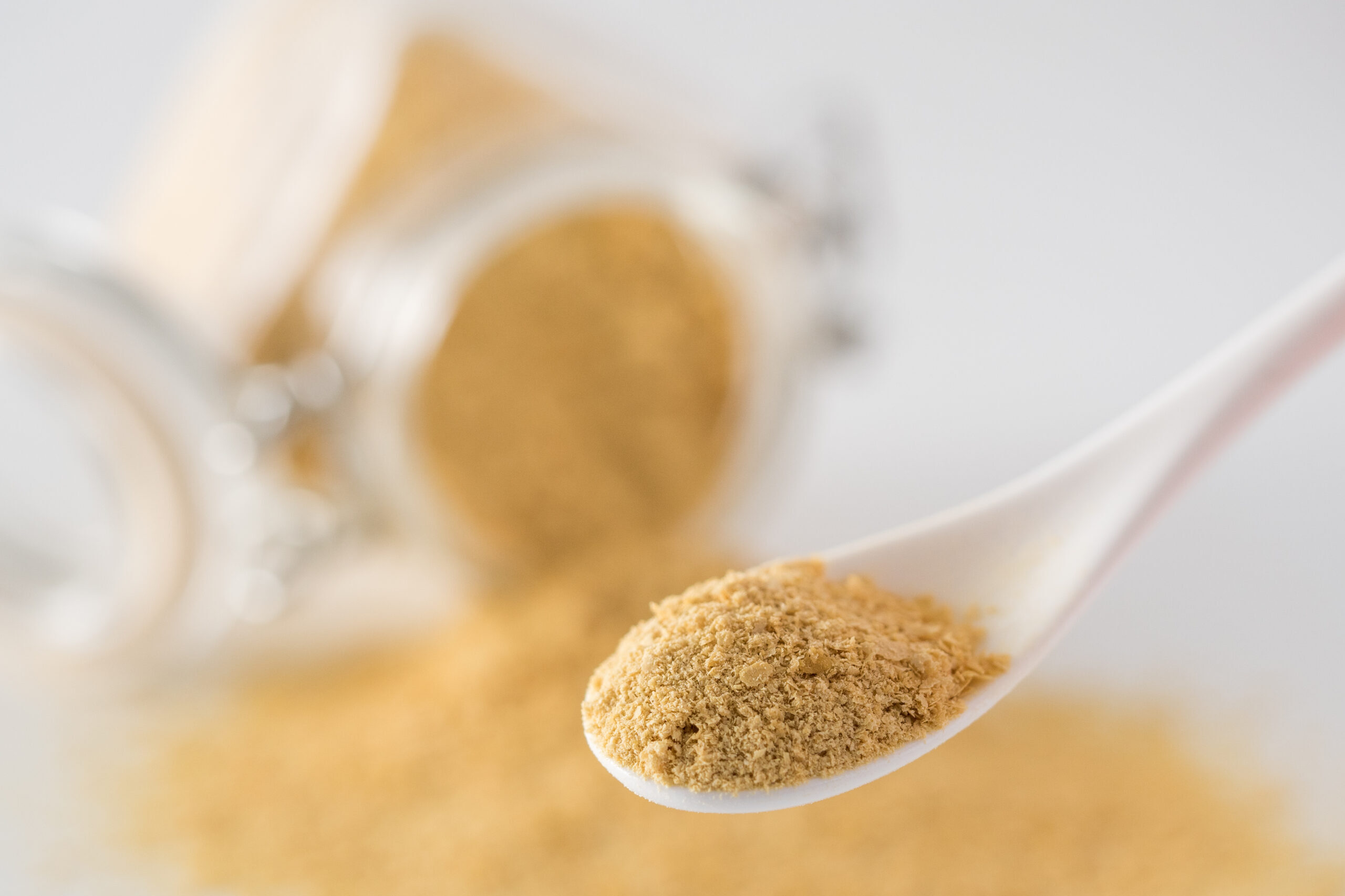 Nutritional yeast background. Nutritional inactive yeast in small spoon and spilled from glass jar on background. Copy space. Nutritional yeast is vegetarian superfood with cheese flavor